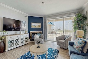 A living room with a TV, sofa, armchair, and a fireplace. - Belmont Towers 410 (Ocean City)