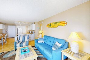 A living room with a blue sofa, striped armchairs, a coffee table, and a wall-mounted lamp. - Gorgeous oceanfront condo with pool, central AC, WiFi, balcony water views (Ocean City)