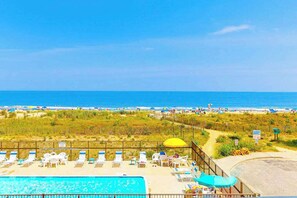 A pool area with lounge chairs and umbrellas, a beach in the background, and a clear sky. - Gorgeous oceanfront condo with pool, central AC, WiFi, balcony water views (Ocean City)