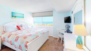 Un dormitorio con cama, escritorio, silla, televisor y ventana con vistas.