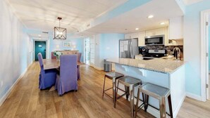A modern kitchen with a central island, bar stools, and a dining area with purple chairs. - Beachfront Condo w/Free WiFi, AC, Private Washer/Dryer, Shared Pool, Water Views (Ocean City)
