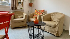 A living room with two beige armchairs, a round coffee table, a red chair, and a potted plant. - Maison Du Grand Sud 2 - Promenade Des Anglais (Nice)
