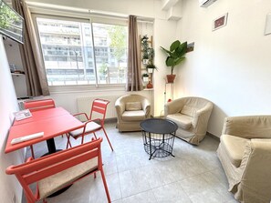 Ein möbliertes Wohnzimmer mit Esstisch, Stühlen, einer Couch, einem kleinen runden Tisch und einem Blumentopf.