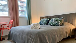 A neatly made bed with rolled towels, a grey headboard, and tropical patterned pillows. - Maison Du Grand Sud 2 - Promenade Des Anglais (Nice)