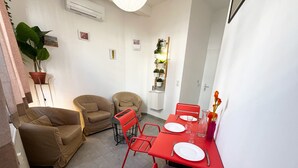 A compact living space with a dining area, two sofas, a red dining table, and a potted plant. - Maison Du Grand Sud 2 - Promenade Des Anglais (Nice)