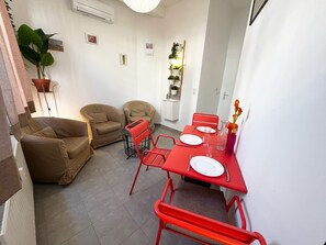 Ein kompakter Wohnraum mit Essbereich, zwei Sofas, einem roten Esstisch und einem Blumentopf.