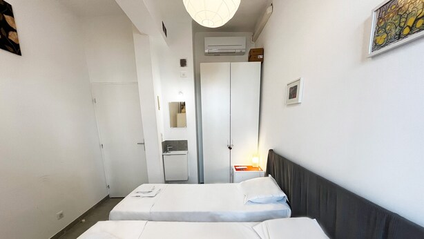 A hotel room with two single beds, a bedside table with a lamp, a mirror, and a door leading to a bathroom. - Maison Du Grand Sud 2 - Promenade Des Anglais (Nice)