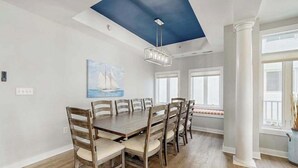 Ein Esszimmer mit einem großen Holztisch, Stühlen, einer Deckenleuchte und einem Gemälde.