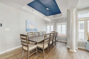 A dining room with a large wooden table, chairs, a ceiling light, and a painting. - Bright, Modern Beach Home Steps From Water w/Ocean Views, Central AC, WiFi, W/D (Ocean City)