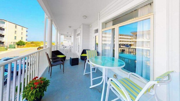 Ein Balkon mit Glastisch und Stühlen, Blick auf einen Pool und einem weißen Geländer.