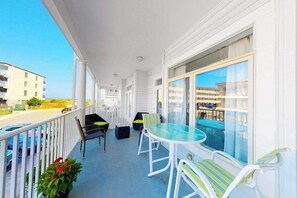 Un balcon avec une table et des chaises en verre, donnant sur la piscine, et une balustrade blanche.
