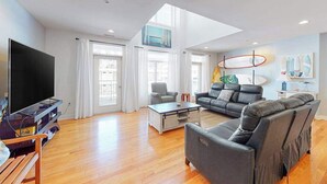 Ein modernes Wohnzimmer mit Fernseher, Ledersofas, einem Couchtisch und einem großen Fenster mit Vorhängen.