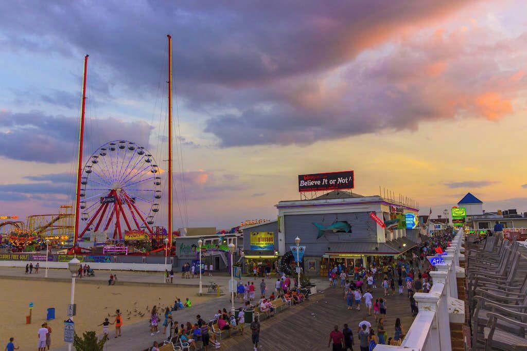 A boardwalk with a Ferris wheel, a building with a shark sign, and a crowd of people.