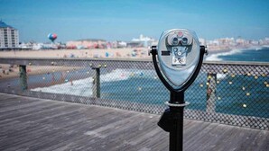 A vintage telescope on a wooden deck overlooking a beach with a fence, ocean, and distant cityscape. - Beach Club 127 A (Ocean City)