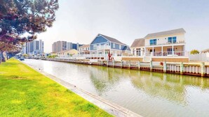 A waterfront property with a dock, a grassy area, and a row of houses along the water. - Beach Club 127 A (Ocean City)