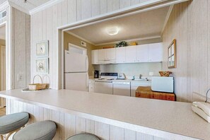 A kitchen with white cabinets, a refrigerator, a coffee maker, and a sink. - Oceanfront Condo near the Boardwalk with Balcony, AC & Shared Outdoor Pool (Ocean City)