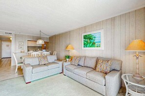 A living room with two sofas, a dining table, a kitchen in the background, and a painting on the wall. - Oceanfront Condo near the Boardwalk with Balcony, AC & Shared Outdoor Pool (Ocean City)