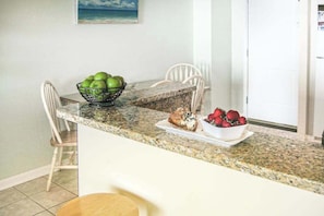 A kitchen counter with a bowl of green apples, a plate of strawberries, and a white chair. - Oceanfront condo with balcony, lovely sunrise view, central AC & pool (Ocean City)