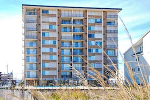 A multi-story hotel with balconies, a swimming pool, and a clear sky. - Oceanfront condo with balcony, lovely sunrise view, central AC & pool (Ocean City)