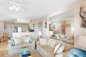 A living room with striped sofas, a coffee table, a kitchen in the background, and a large mirror. - Oceanfront condo with balcony, lovely sunrise view, central AC & pool (Ocean City)