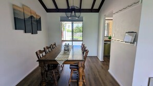 A dining area with a wooden table and chairs, a chandelier, and a view through a glass door. - Welcoming 3-Bed House with Large Backyard (Mandurah)