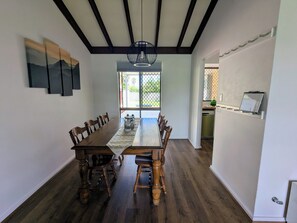 A dining area with a wooden table and chairs, a chandelier, and a view through a glass door. - Welcoming 3-Bed House with Large Backyard (Mandurah)