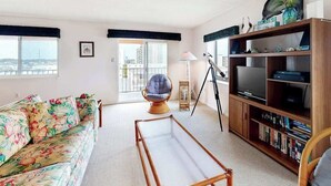 Un salon comprenant un canapé, un fauteuil, une bibliothèque, un téléviseur et un balcon avec vue.
