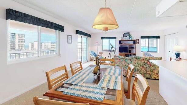 Un espace repas avec une table et des chaises en bois, une lampe suspendue et une vue sur la ville grâce à de grandes fenêtres.