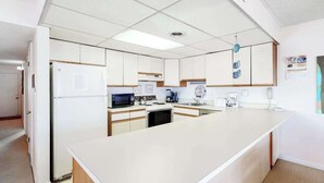Une cuisine moderne avec des meubles blancs, un îlot central, un four à micro-ondes et une machine à café.