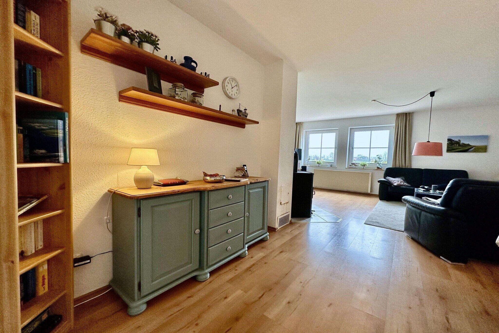 Ein Wohnzimmer mit Holzboden, einem grünen Schrank, einem schwarzen Sofa und einem Fenster mit Blick.