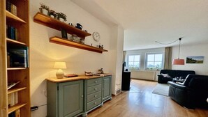 Una sala de estar con piso de madera, un mueble verde, un sofá negro y un ventanal con vistas.