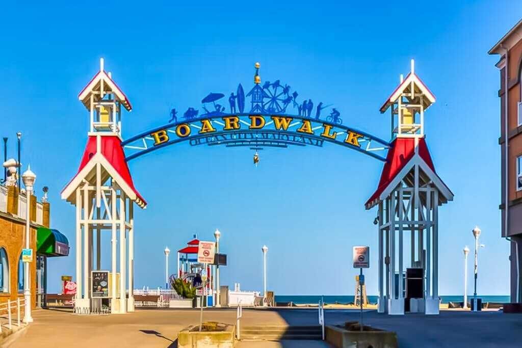 A boardwalk entrance with a sign, lamp posts, and a clear sky.
