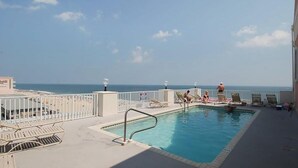 A pool area with lounge chairs, a pool, and a view of the ocean. - Condo in an oceanfront building with side ocean view, pool, gym & garage parking (Ocean City)