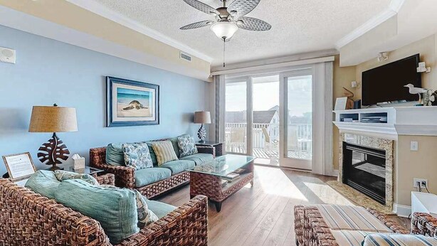 A living room with wicker furniture, a ceiling fan, a fireplace, and a large window. - Condo in an oceanfront building with side ocean view, pool, gym & garage parking (Ocean City)