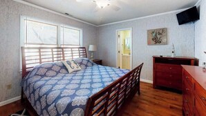 Een slaapkamer met een bed, een houten dressoir, een plafondventilator en een aan de muur bevestigde televisie.