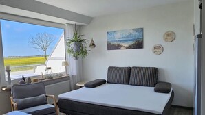 Une chambre à coucher comprenant un lit, un bureau, une chaise, une fenêtre donnant sur des champs et un réfrigérateur.