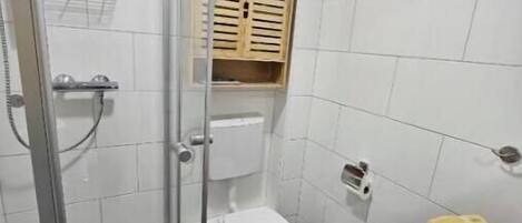 A bathroom with a glass shower enclosure, a toilet, a sink, and a wooden cabinet.