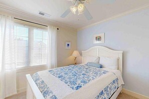 Ein Schlafzimmer mit einem Bett, einem Deckenventilator, einem Fenster mit Vorhängen und einem Wandbild.