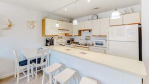 A compact kitchen with a central island, white cabinetry, pendant lighting, and a clock on the wall. - Siesta Villa 304N (Ocean City)