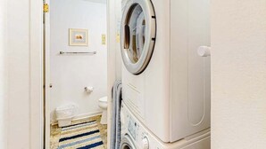 A laundry room with a stacked washer and dryer, a striped rug, and a toilet in the background. - Siesta Villa 304N (Ocean City)