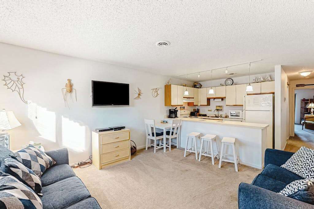 Ein modernes Wohnzimmer mit Sofa, Fernseher, Küchenzeile mit Bar und Esstisch mit Stühlen.