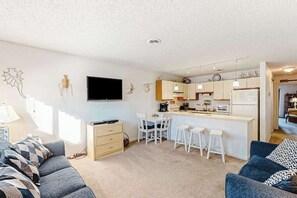 Ein modernes Wohnzimmer mit Sofa, Fernseher, Küchenzeile mit Bar und Esstisch mit Stühlen.