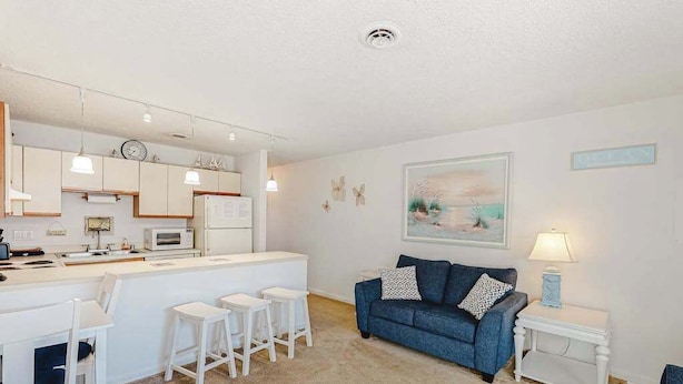 A compact living space with a kitchenette, a blue sofa, a small dining area, and a painting on the wall. - Siesta Villa 304N (Ocean City)