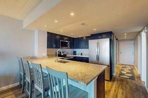 A modern kitchen with dark cabinets, a granite countertop, a stainless steel refrigerator, and a built-in microwave. - Incredibly Convenient Beach Condo w/Balcony, W/D, A/C, Shared Pools, Gym, Tennis (Ocean City)