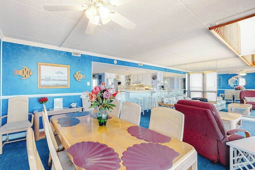 Quarto com parede azul, mesa de jantar com cadeiras, poltrona vermelha e ventilador de teto.