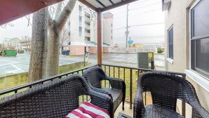 A covered balcony with wicker furniture, a view of a building, and a tree. - First-Floor, Ocean Block Condo with Patio, AC, WiFi & Laundry - Steps to Beach (Ocean City)