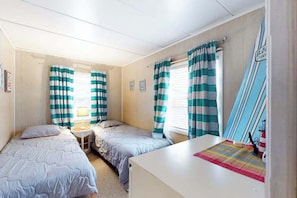 A room with two beds, a small table with a lamp, and a surfboard decoration. - First-Floor, Ocean Block Condo with Patio, AC, WiFi & Laundry - Steps to Beach (Ocean City)