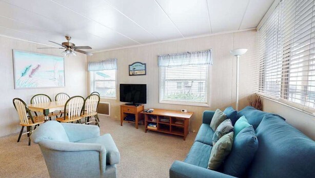 A living room with a ceiling fan, a television, a dining table with chairs, a sofa, and a lamp. - First-Floor, Ocean Block Condo with Patio, AC, WiFi & Laundry - Steps to Beach (Ocean City)
