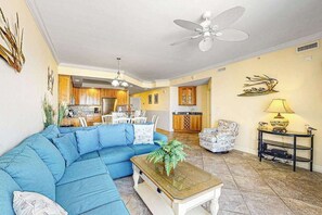 A living room with a blue sofa, a coffee table, a lamp, and a ceiling fan. - Belmont Towers 305 (Ocean City)