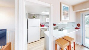 A modern kitchen with white cabinetry, a central island, and a dining area with a wooden bench. - Beach Club  135 D (Ocean City)